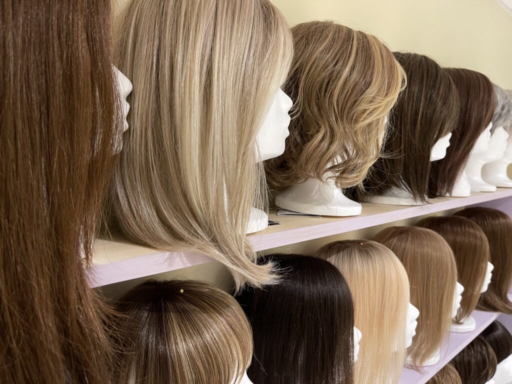 Shelves of wigs and hair toppers in blonde and brunette shades on mannequin heads at Foxy Locks